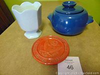 Front view of the white planter, blue soup bowl with lid, and red trivet on a table.