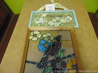 Photo showing the two painted glass items: a framed cardinal bird glass picture and a rectangular floral welcome sign