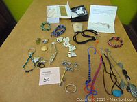 Overview of all jewelry items spread on a table including necklaces, bracelets, key chains, and boxed jewelry