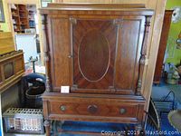 Front view of the china cabinet showing the decorative wood inlay door, turned columns, and drawer below.