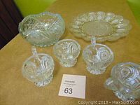 Photo showing clear glass bowl, small pitcher, and three cups with decorative pressed patterns on a table.