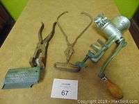 Front angle of all four items: ice tongs, ice shaver, meat grinder and ear tattoo tool on a table.