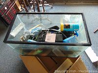 Photo of empty 10 gallon glass aquarium tank viewed from above, showing some accessories inside the tank including water filter, water conditioner, and a decorative plant.