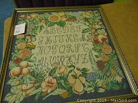 Front view of the framed tapestry showing the full embroidered alphabet and vibrant floral and fruit border.