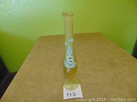 Front view of the tall satin glass bud vase showing hand-painted white floral decoration with some orange highlights on a frosted yellow background.