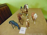 Five Breyer model horses displayed on a tabletop in a posed standing formation: two adult mares and three smaller foals in various colors.