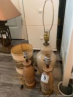 Photo showing three lamps: beige ginger jar lamp with harp, two smaller wine bottle lamps, all on floor with electrical cords visible.