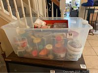Wide photo showing a large translucent plastic bin filled with bead containers and supplies on a table.