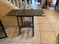 Full view of Hi-Low utility table showing three-section drop leaf top and metal base with wheels.