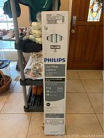 Full view of unopened Philips Cool White Supreme fluorescent light tubes 10-pack in original packaging standing upright on tiled floor near entrance door.