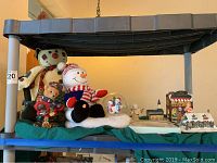 Overview photo showing all items together including snowman plush, elf plush, and miniature buildings with snow detailing.