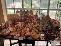 Overview of the large collection of Christmas tabletop and tree trim decorations including Santa figurines, angels, wooden bead garlands, cups, and gold glitter ornaments on a table.