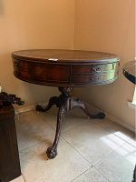 Full side view of antique round wooden side table with carved pedestal and lion paw feet on tile floor.