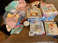 Photo showing assembled lot on a table with four boxed puzzles, books, doll clothes, and toys.