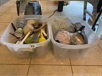 Two large plastic bins on tiled floor filled with assorted kitchen utensils, pots, and cookware items, showing overall lot contents.