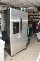 Full view of the stainless steel side-by-side refrigerator showing front and side in garage setting.