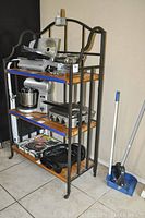 Front view of the metal and wood bakers rack fully stocked with kitchen appliances and cookware, showing three wooden shelves with top curved metal frame.