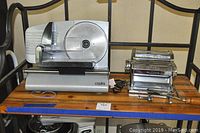 Side view of Cooks electric meat slicer and Imperia pasta maker placed on wooden shelf.