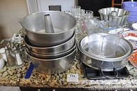 Side view of stacked aluminum pans and mixing bowls on countertop alongside glass and plastic kitchenware.