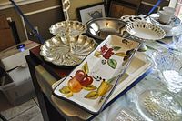 Photo showing 2-tier silverplate server, rectangular ceramic serving plate with painted fruit, and silverplate bowl in background on table with other dishes.