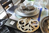 Photo showing Harmony House serving plates, bowl, teacups and saucers stacked, with the Royal Worcester plate on top and the warm plates holder in front on a dark table.