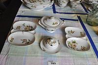 Five pieces of Lynmore Golden Rose fine china including two oval trays, a sugar bowl with lid, and a small bowl with lid arranged on a table with cloth.