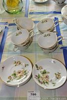 Tea cups and plates arranged on a tablecloth showing golden rose floral pattern and gold trim.