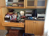 Wide view of desk and shelving showing assorted books, two clocks, office supplies in open drawer, briefcase below desk.