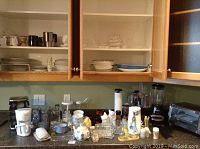 Kitchen countertop and upper cupboards displaying small kitchen appliances including toaster oven, blender, food processor, glassware, dishes, and various kitchen items.