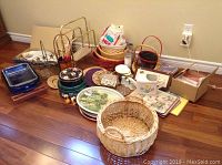 View of baskets, metal fish tray, blue Pyrex dishes, tin trays, and assorted kitchenware items on wooden floor.