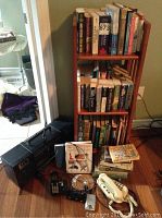 Wooden bookshelf filled with assorted books and electronic items on floor nearby