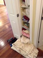 View of closet floor and shelves with folded linens including floral quilted bedspread stacked on floor and other linens on shelves.