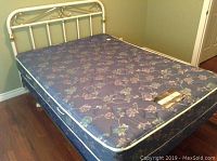 Photo of the mattress and cream colored metal headboard with vertical bars and rounded rails.