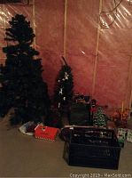 Photo shows two artificial Christmas trees, one large around 6 feet and one smaller in a pot, along with various holiday decorations, ceramic Christmas tree decoration, and candles arranged on floor.