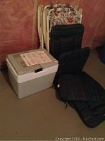 Koolatron electric cooler with owner's manual on top, two folding chairs with cushions leaning against wall.