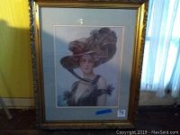 Full view of framed artwork showing woman in large hat with gilded frame