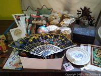Photo showing multiple items including unopened candles, decorative fan, religious literature, wooden box, metal windmill, and metal star frames.