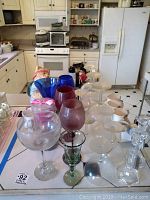 Kitchen counter with assorted glassware including colored wine goblets, cocktail glasses, coffee cups, crystal candlesticks, and Clay Art cookie jar