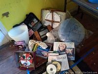 Photo shows plastic trash cans, boxed software, one night stand pillow wrapped in plastic, and assorted items including a decorative carousel face item and a storage bin.