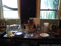 Full view of folding table with various kitchen items including plates, glass jars, copper pot, decorative plates, and electrical items.