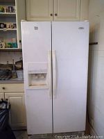Full view of white Whirlpool side-by-side refrigerator with freezer and built-in water/ice dispenser, seen in kitchen setting.