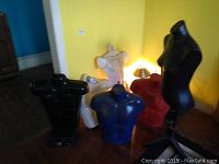 Group of six plastic mannequin torsos in various colors arranged against a yellow wall showing different torso styles.