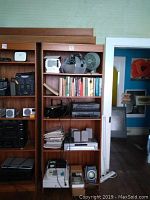 Full view of teak shelf with many electronics, books, and fan