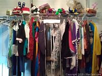 Full view of hanging costumes in various colors and styles and top shelf with hats and accessories