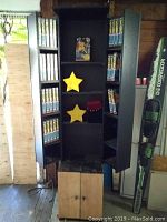 Full view of black wooden cabinet with double doors open, showing shelves filled with VHS tapes and collectible star boxes.