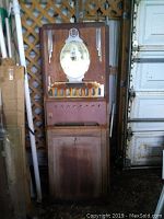 Full view of vintage cigarette vending machine standing next to lattice and garage door showing overall condition and height.