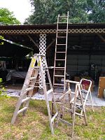 Photo of five ladders outside under carport: two wood ladders, two metal step ladders including a bent one, and a small 3-step ladder.
