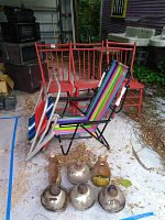 Two beach folding chairs with colorful striped fabric in front of the three red wooden chairs and five oil tiki lamps on the ground.