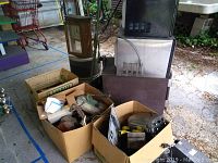Boxes with assorted electrical components, vintage metal detectors, and several microwaves stacked behind.