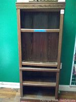 Front view of the brown woodgrain finished five-shelf bookcase against a green wall.
